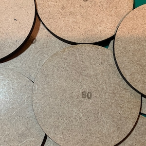 May include: A close-up of a stack of six brown, round, wooden bases with the number "60" printed on each base.
