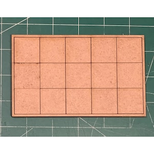 May include: A rectangular, light brown wooden tile with a grid pattern of 15 squares. The grid lines are black. The tile is on a green surface.