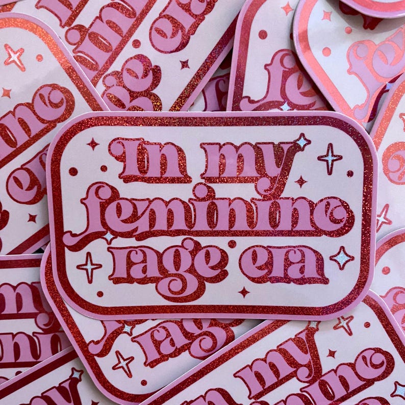 May include: Pink and red glitter sticker with the text "In my feminine rage era" in a retro font.