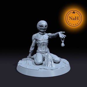 May include: A gray 3D printed miniature of a humanoid figure wearing a helmet and bandages. The figure is kneeling and holding a small object in its outstretched hand.