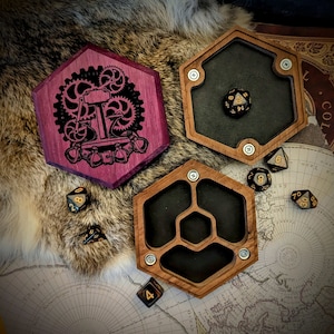 May include: A set of three wooden dice trays with a hexagonal shape. The trays are made of dark wood with black felt lining. The trays are designed to hold dice for role-playing games. One tray features a purple and black design with a steampunk-inspired image of a gear-driven machine.