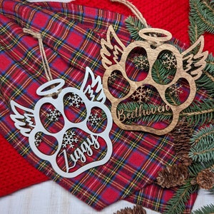 May include: Two wooden paw print ornaments with angel wings and snowflakes. The ornaments are personalized with the names "Ziggy" and "Beethoven".