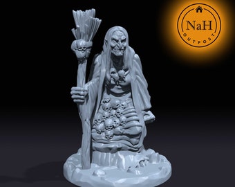 May include: A gray, detailed miniature figurine of a witch holding a staff with a skull at the top. The witch is wearing a long robe and has a skull-shaped necklace. The base of the figurine is a circular platform with a skull on it.