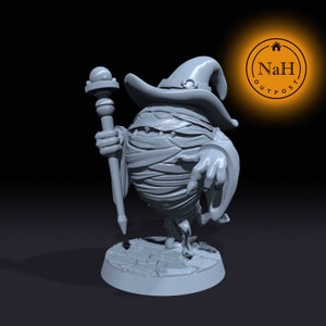 Puede incluir: Una miniatura impresa en 3D de color gris de una momia que lleva un sombrero de mago y sostiene un bastón. La momia está de pie sobre una base redonda.