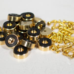 May include: A pile of gold-colored speaker isolation feet with black rubber pads. There are also a number of gold-colored screws with round heads.