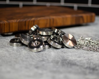 May include: A close-up of a pile of silver metal round furniture feet with black rubber inserts. A pile of silver screws is in the background.