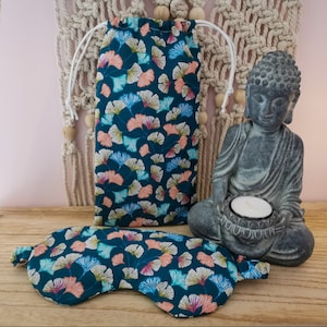 May include: A teal blue sleep mask with a floral pattern and a matching drawstring bag. The bag has a white drawstring and is filled with a teal blue fabric with a floral pattern.