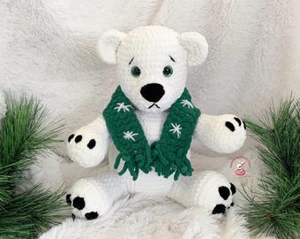 Può includere: Orso polare bianco all'uncinetto con una sciarpa verde con fiocchi di neve bianchi. L'orso ha occhi neri e un naso nero.