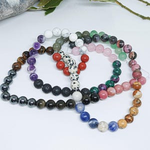 Pode incluir: Uma cole&ccedil;&atilde;o de pulseiras de contas em v&aacute;rias cores e tipos de pedra. As pulseiras incluem contas em tons de preto, castanho, roxo, branco, vermelho, rosa, verde e azul. As contas s&atilde;o enfiadas em cord&otilde;es el&aacute;sticos.