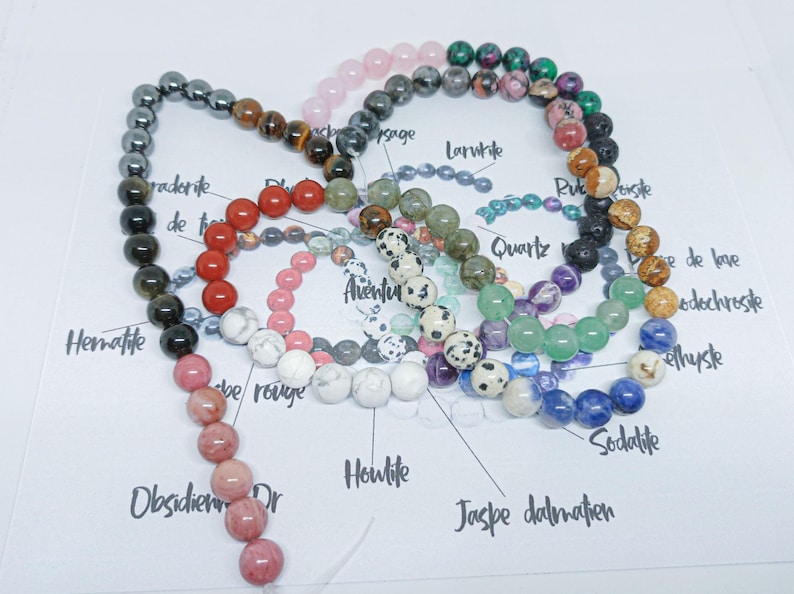 Pode incluir: Uma cole&ccedil;&atilde;o de pulseiras de contas em v&aacute;rias cores e tipos de pedra, incluindo hematita, quartzo e sodalita. As contas s&atilde;o enfiadas, mostrando uma variedade de texturas e tons, de pretos profundos a azuis e rosas vibrantes.