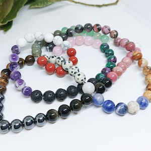 Pode incluir: Uma cole&ccedil;&atilde;o de pulseiras de contas em v&aacute;rias cores, incluindo branco, preto, vermelho, rosa e azul. As pulseiras s&atilde;o feitas de diferentes tipos de pedras e contas, mostrando uma variedade de texturas e padr&otilde;es.