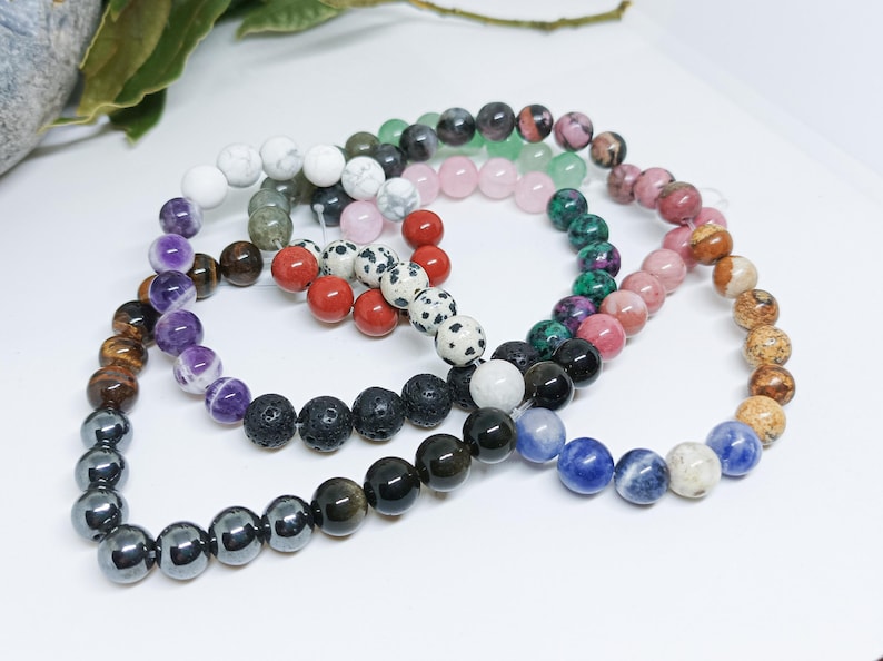 Pode incluir: Uma cole&ccedil;&atilde;o de pulseiras de contas em v&aacute;rias cores, incluindo branco, preto, vermelho, rosa e azul. As pulseiras s&atilde;o feitas de diferentes tipos de pedras e contas, mostrando uma variedade de texturas e padr&otilde;es.
