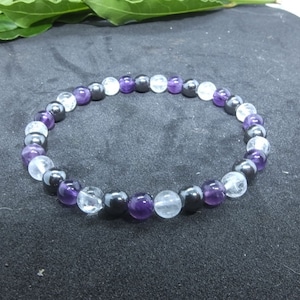 Peut inclure: Un bracelet de perles rondes violettes, transparentes et noires. Les perles mesurent environ 0,8 cm de diamètre. Le bracelet est présenté sur une surface sombre. Les pierres polies créent un motif de couleurs contrastées.