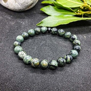 Pode incluir: Um bracelete de pedras preciosas pretas e verdes com contas redondas. O bracelete é feito de pedras naturais e tem um padrão único.