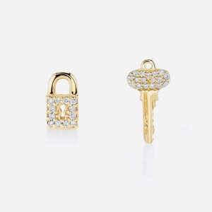 May include: A pair of gold earrings, one shaped like a padlock and the other shaped like a key, both adorned with sparkling clear crystals.