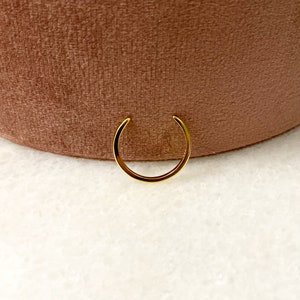 Op de afbeelding: Een gouden neusring met een simpel, afgerond ontwerp.