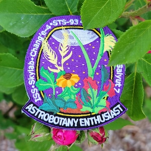 May include: Purple embroidered patch with a space shuttle, plants, and a moon. The text reads "ISS - Skylab - Challenger - STS-93 - Astrobotany Enthusiast".