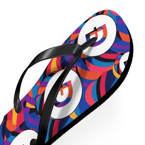 May include: A pair of black flip-flops with a colorful abstract pattern and a white circle with a letter "G" in the center.
