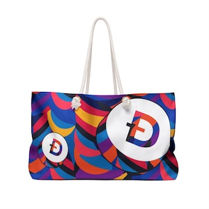 May include: A colorful tote bag with a white circle featuring the letter "D" in a stylized font. The bag has a rope handle and a blue, red, yellow, and purple abstract pattern.
