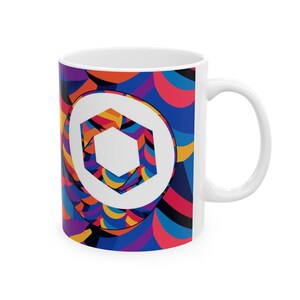 May include: White ceramic mug with a colorful geometric design featuring a white hexagon logo in the center. The design includes shades of blue, red, yellow, and purple.