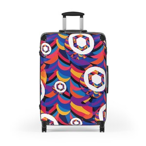 May include: A rolling suitcase with a vibrant, abstract design. The pattern features overlapping shapes in shades of blue, orange, yellow, and purple, with white geometric accents. The suitcase has a retractable handle and black wheels.