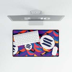 May include: A white keyboard and mouse are on a colorful desk mat with a geometric pattern. The mat features a repeating logo with three blue lines on a white circle. The mat is on a white surface.