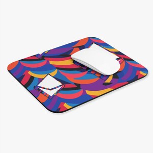 May include: A colorful mouse pad with a geometric pattern in shades of red, blue, yellow, and purple. A white computer mouse is on top of the mouse pad.