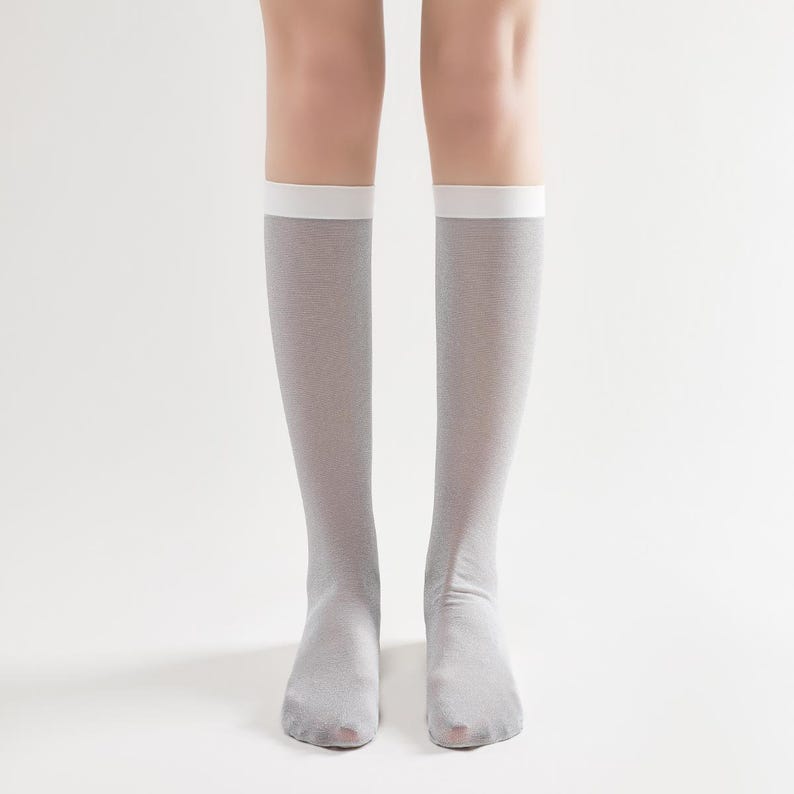 May include: A pair of knee-high socks in a light gray color with a white band at the top. The socks are made of a thin, sheer material. The image is a close-up of the socks, showing the details of the fabric and the fit.