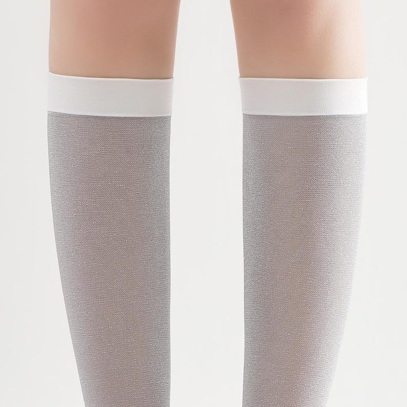 May include: A pair of knee-high socks in a light gray color with a white band at the top. The socks have a subtle shimmer and a textured appearance. The background is plain white.