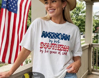 May include: White t-shirt with the text "AMERICAN by birth SOUTHERN by the grace of God" in red, white, and blue. The shirt is paired with denim shorts and a straw cowboy hat. An American flag is in the background.