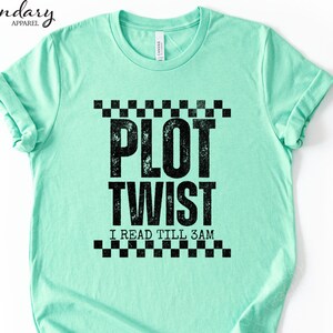 May include: Mint green t-shirt with the text "PLOT TWIST" in large, distressed black letters, with "I READ TILL 3AM" below. The design is framed by a black and white checkered pattern. The shirt has short sleeves and a crew neck.