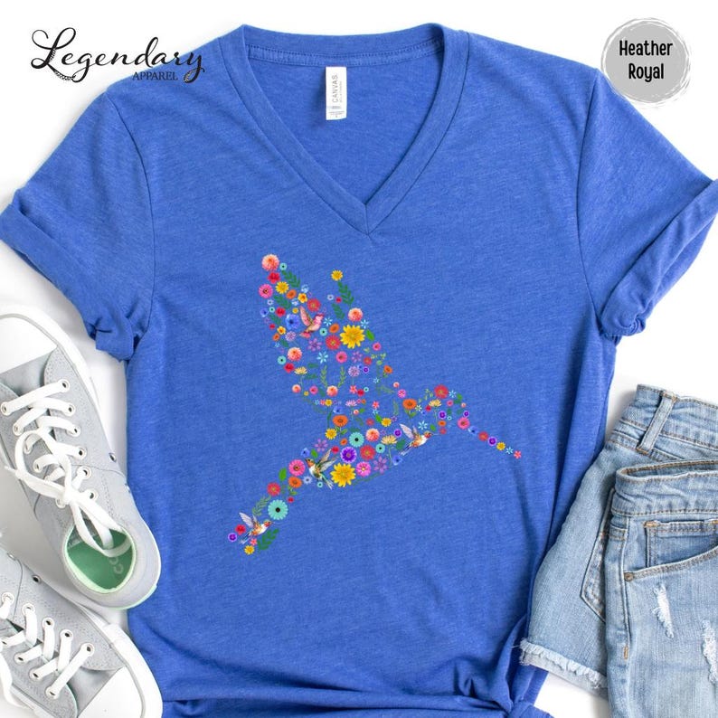 May include: A heather royal blue v-neck t-shirt with a hummingbird design made of colorful flowers. The hummingbird is facing left and is outlined with flowers.