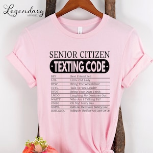 A pink t-shirt with a humorous text that reads "SENIOR CITIZEN TEXTING CODE" printed on it.