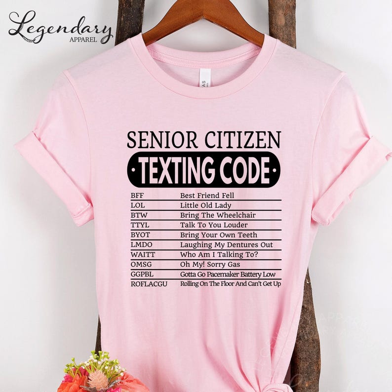 A pink t-shirt with a humorous text that reads "SENIOR CITIZEN TEXTING CODE" printed on it.