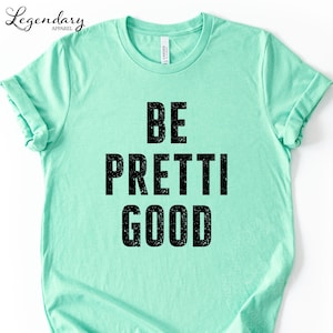 May include: A mint green t-shirt with the words "BE PRETTI GOOD" printed in large, black, distressed font. The shirt has short sleeves and a crew neck. The brand name "Legendary Apparel" is printed in the upper left corner.