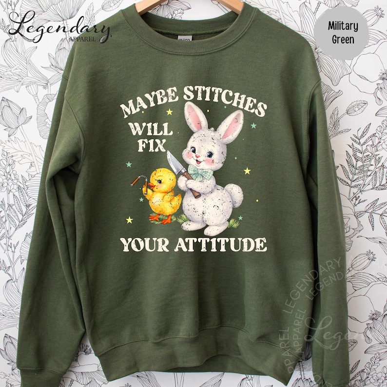 A green sweatshirt with a cartoon image of a rabbit and a duck, along with the text "MAYBE STITCHES WILL FIX YOUR ATTITUDE" printed on it.