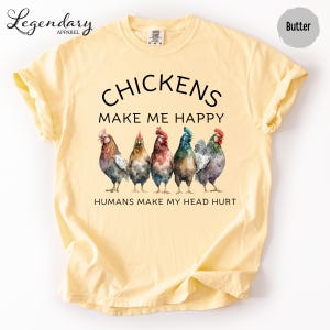 May include: Butter-colored t-shirt with the text "CHICKENS MAKE ME HAPPY HUMANS MAKE MY HEAD HURT". The shirt features a watercolor illustration of six colorful chickens. The shirt is from Legendary Apparel.