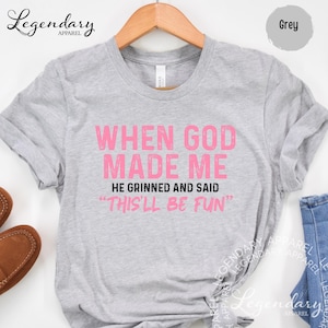 A grey t-shirt with a humorous text printed on it, hanging on a wooden hanger.
