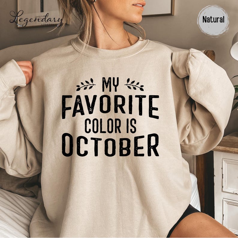 A woman wearing a beige sweater with the text "My favorite color is October" printed on it.