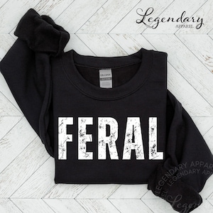 A black sweatshirt with the word "FERAL" printed in white text on it, laid out on a white background.