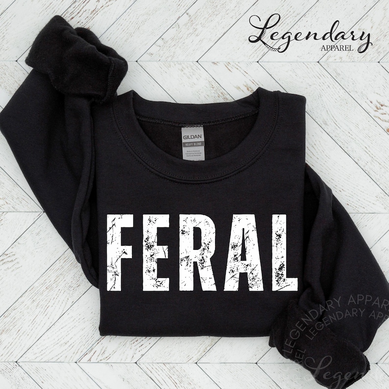 A black sweatshirt with the word "FERAL" printed in white text on it, laid out on a white background.