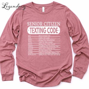 A pink long-sleeved shirt with a humorous text printed on it, which appears to be a list of rules or guidelines for senior citizens when it comes to texting.