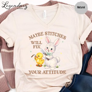 a white t-shirt with a printed design of a rabbit and a duck holding a knife, accompanied by the text "MAYBE STITCHS WILL FIT YOUR ATTITUDE".