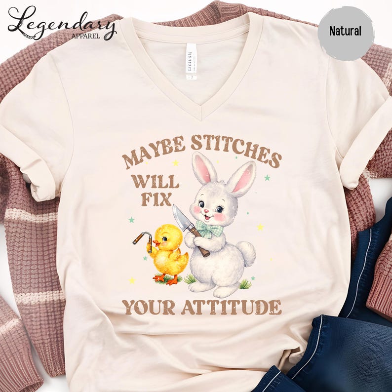 a white t-shirt with a printed design of a rabbit and a duck holding a knife, accompanied by the text "MAYBE STITCHS WILL FIT YOUR ATTITUDE".