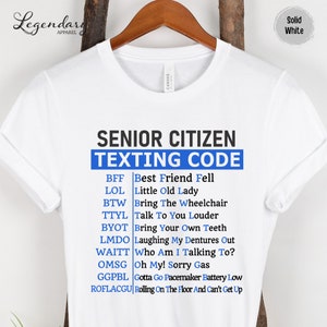 May include: White t-shirt with blue text that reads "Senior Citizen Texting Code" and a list of abbreviations and their meanings. The abbreviations are: BFF, LOL, BTW, TTYL, BYOT, LMDO, WAITT, OMSG, GGPBL, ROFLACGU.