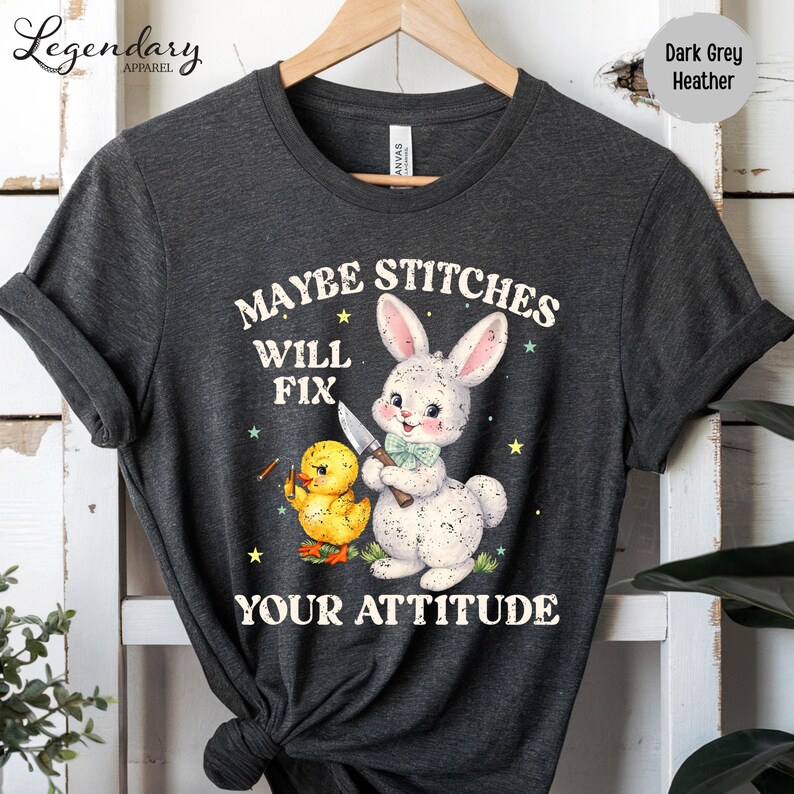 A gray t-shirt with a graphic design featuring a rabbit and a duck, along with the text "MAYBE STITCHES WILL FIX YOUR ATTITUDE".