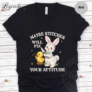 The image is a black t-shirt with a graphic design featuring a rabbit and a duck holding a knife, along with the text "MAYBE STITCHS WILL FIT YOUR ATTITUDE".
