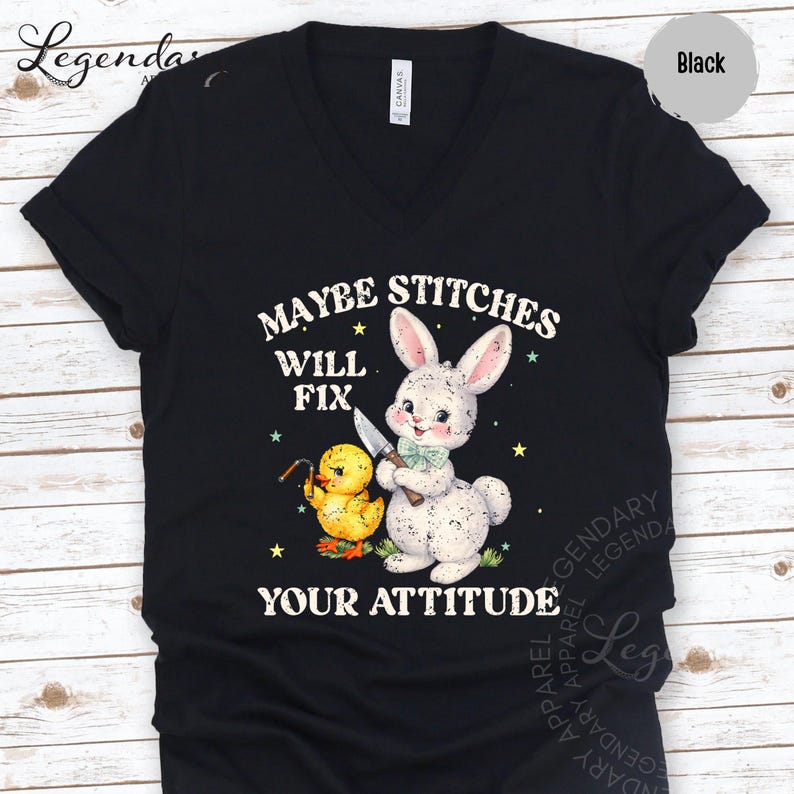 The image is a black t-shirt with a graphic design featuring a rabbit and a duck holding a knife, along with the text "MAYBE STITCHS WILL FIT YOUR ATTITUDE".