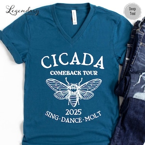 May include: Deep teal V-neck t-shirt with white text and a cicada graphic. The text reads "CICADA COMEBACK TOUR 2025 SING DANCE MOLT". The graphic features a detailed outline of a cicada.