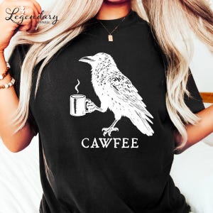 A person wearing a black t-shirt with a white graphic design depicting a bird holding a coffee cup.